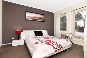 A bedroom with a bed, a nightstand, a lamp, a window with curtains, and a picture on the wall. - Mclaren Vale Studio Apartments (Adelaide)