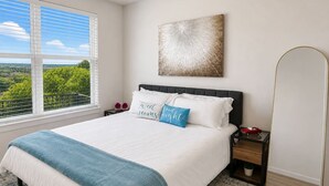Um quarto com uma cama, mesa de cabeceira, espelho e janela com vista.