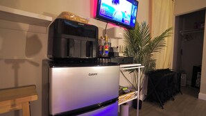 Eine kompakte Küchenzeile mit einem Galanz-Kühlschrank, einer Kaffeemaschine und einem flachbildfernseher an der Wand.