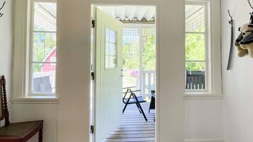 A hallway leading to a porch with a wooden chair, a doormat, and a coat rack with a stuffed animal.