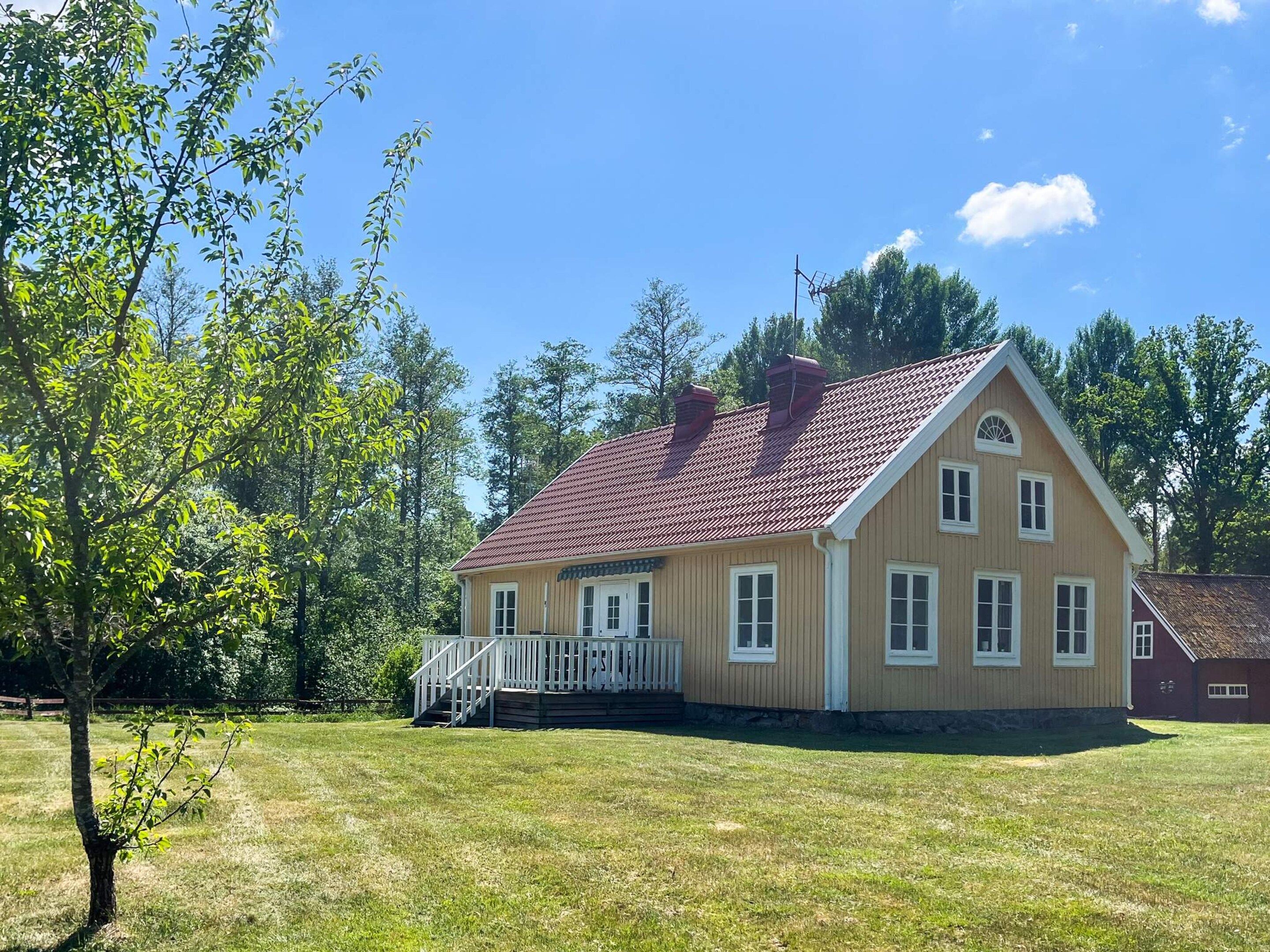 A two-story house with a red-tiled roof, a front porch, and a grassy yard.