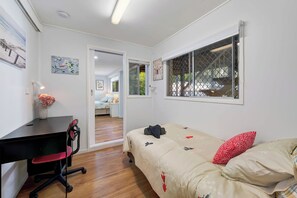 A bedroom with a bed, a desk, a chair, a window with a view, and a door leading to another room. - Verney Beachside Getaway (Kings Beach)