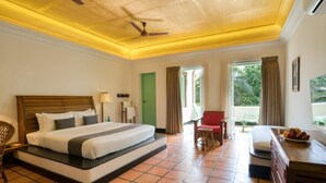A hotel room with a large bed, a desk with a chair, a small table with food, and a view of greenery outside. - Hotel Mango Hill (Vanur)
