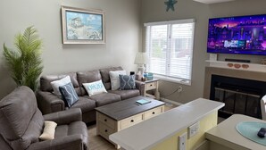 Een woonkamer met een bruine leren bank, een klein bijzettafeltje, een televisie en een open haard.