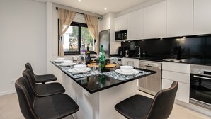 A modern kitchen with a central island, white cabinetry, and a dining area with black chairs. - Concei Sol Modern Apartment (Tavira)