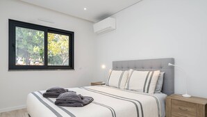 A bedroom with a bed, bedside table, lamp, and window. - Concei Sol Modern Apartment (Tavira)