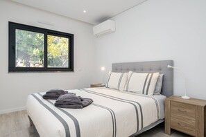 A bedroom with a bed, bedside table, lamp, and window. - Concei Sol Modern Apartment (Tavira)