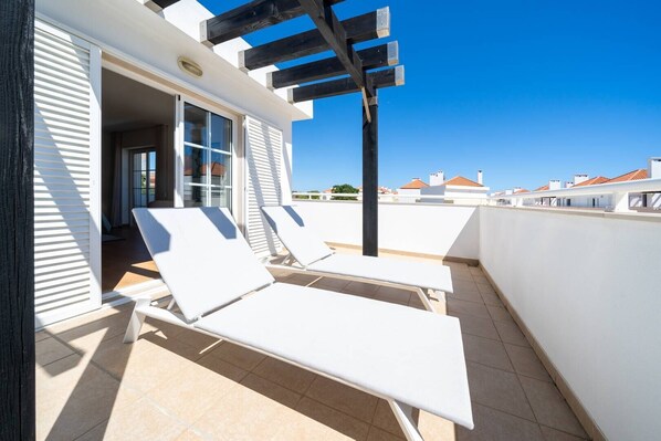 Une terrasse sur le toit, dotée de chaises longues blanches, d’une pergola et offrant une vue sur les autres bâtiments.