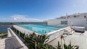 En pool på taget med frit vue over havet, en moderne bygning og en trappe til poolområdet.