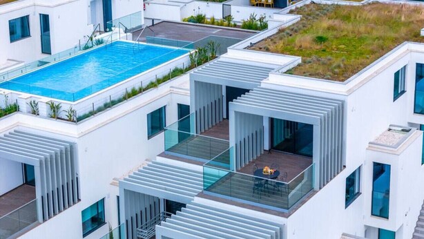 Un edificio moderno de varios pisos con piscina en la azotea, balcones de vidrio y jardín en la terraza.