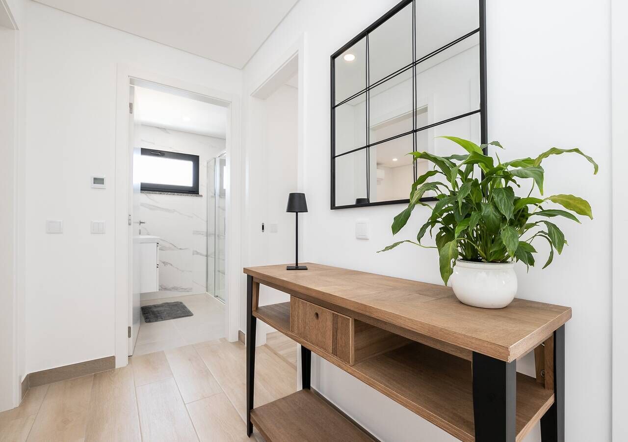 A hallway with a wooden console table, a potted plant, and a mirror on the wall.
