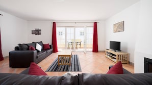 Ein Wohnzimmer mit einer Couch, einem Fernseher, einem kleinen Tisch und einer Schiebetür zu einem Außenbereich.