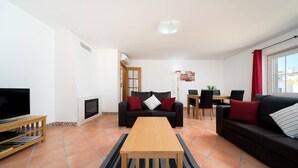 Ein Wohnzimmer mit Fernseher, Sofa, Couchtisch, Kamin, Essbereich und einem Fenster mit Vorhängen.