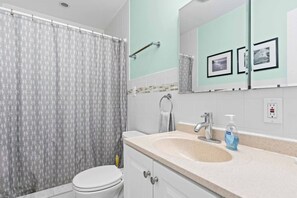 Une salle de bain comprenant des toilettes, un rideau de douche, un lavabo avec un miroir au-dessus et un flacon de savon pour les mains.