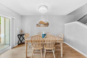 A dining area with a chandelier, wooden chairs, a table, and a wall-mounted artwork. - Beautiful Cape Canaveral Townhouse: Patio, BBQ Grills + Balcony 🌺 (Cape Canaveral)
