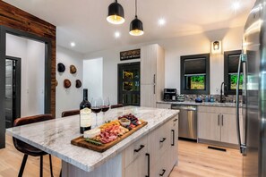 A modern kitchen with a marble island, stainless steel appliances, and a wine bottle. - Brand New Build! Cabin in fabulous Ellijay; Fireplace, Hot tub, Firepit, Pool! (Ellijay)