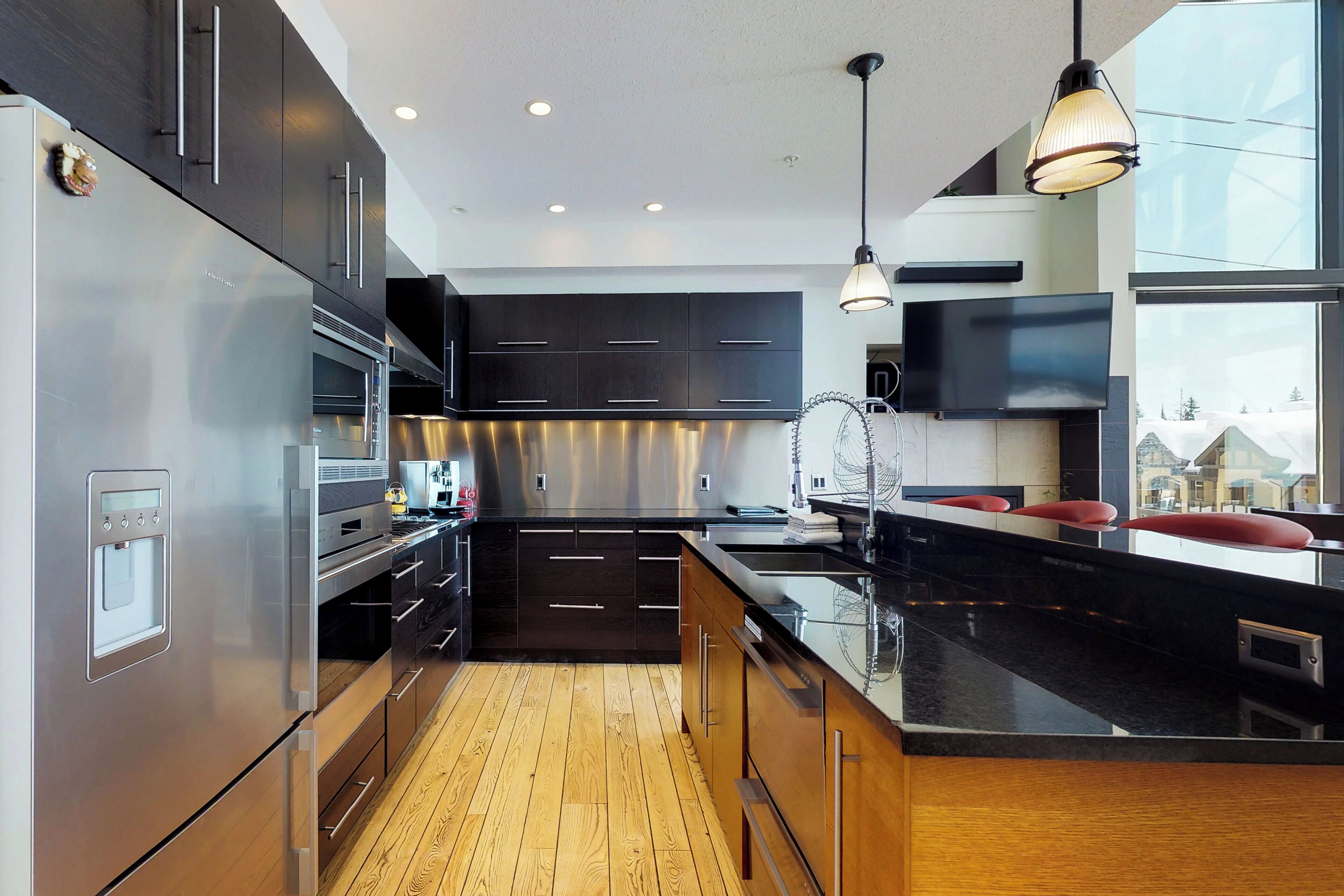 A modern kitchen with dark cabinetry, stainless steel appliances, and a wooden floor.