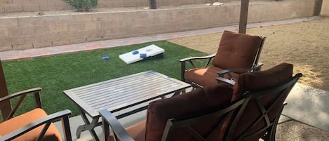 Une terrasse extérieure avec une table et des chaises, un petit coin de gazon artificiel et un mur de briques en arrière-plan.