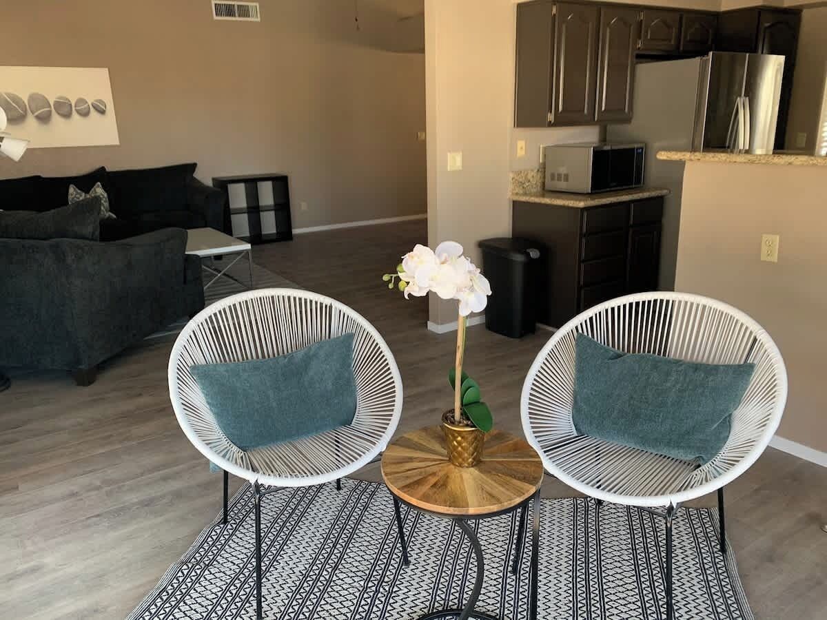 A living room with two white wicker chairs, a small round table, and a potted orchid.