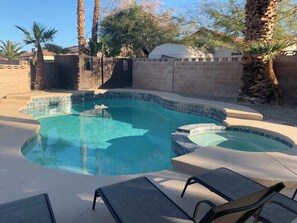 A swimming pool with a curved design, surrounded by a concrete deck and palm trees. - Relaxing Retreat - 5 miles from strip! (Henderson)