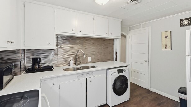 A compact kitchen with white cabinets, a built-in washing machine, a microwave, and a sink. - Leavenworth Apartment (Omaha)
