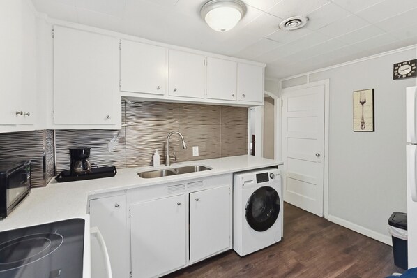 A compact kitchen with white cabinets, a built-in washing machine, a microwave, and a sink. - Leavenworth Apartment (Omaha)