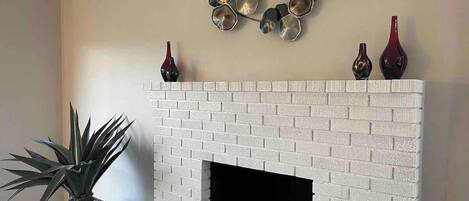 A white brick fireplace with a black firebox, a potted plant, and decorative vases on the mantel.