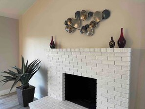 A white brick fireplace with a black firebox, a potted plant, and decorative vases on the mantel. - Trendy and  Tranquil (Las Vegas)