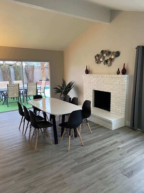A dining area with a white table and black chairs, a white brick fireplace, and a view of the outdoors. - Trendy and  Tranquil (Las Vegas)
