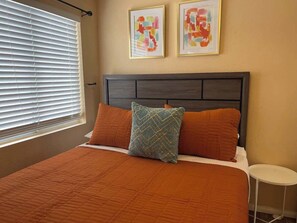 A bedroom with a bed, two pillows, a nightstand, and two abstract paintings on the wall. - Hideaway Haven: Your Retreat with Pool & Hot Tub (North Las Vegas)