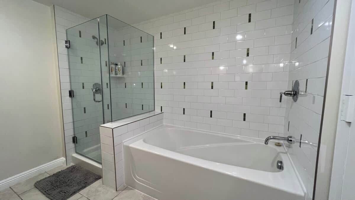 Een badkamer met een douchecabine van glas, een witte badkuip en witte betegelde wanden met zwarte accenten.