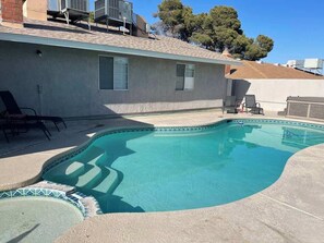 A swimming pool with a tiled edge, a patio area with chairs, and a building with a sloped roof. - Inviting, Open Floor Plan with Pool/Spa (Las Vegas)