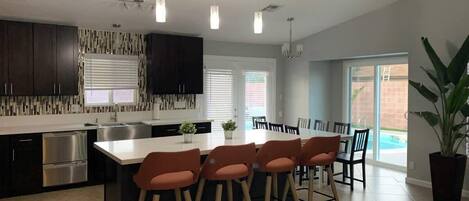 Une cuisine moderne avec des meubles de couleur sombre, un îlot central, des tabourets de bar et des luminaires suspendus.