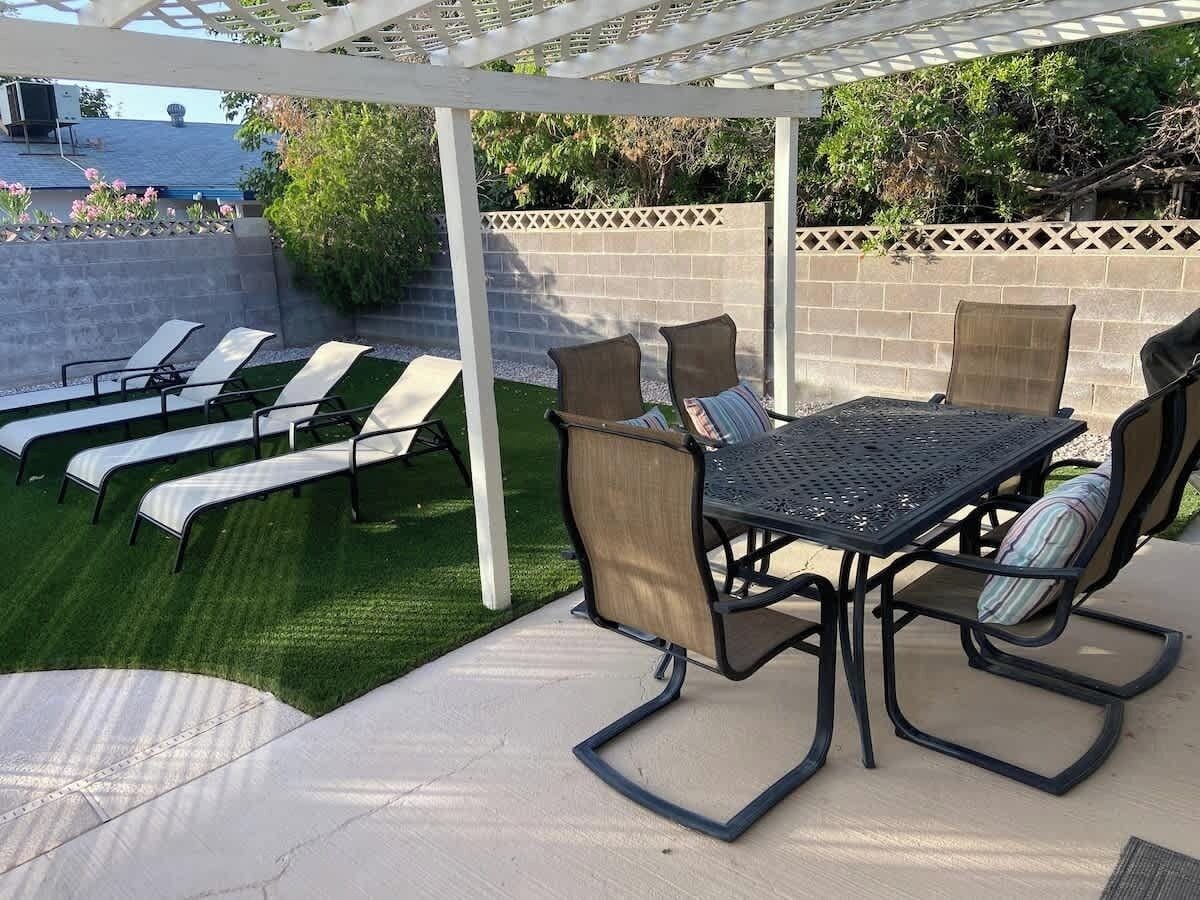 A patio with a table and chairs, a white pergola, and a lawn.