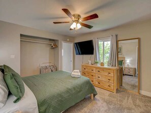 Ein Schlafzimmer mit Bett, einem Holzschrank, einem Deckenventilator, einem Fernseher und einem Spiegel.