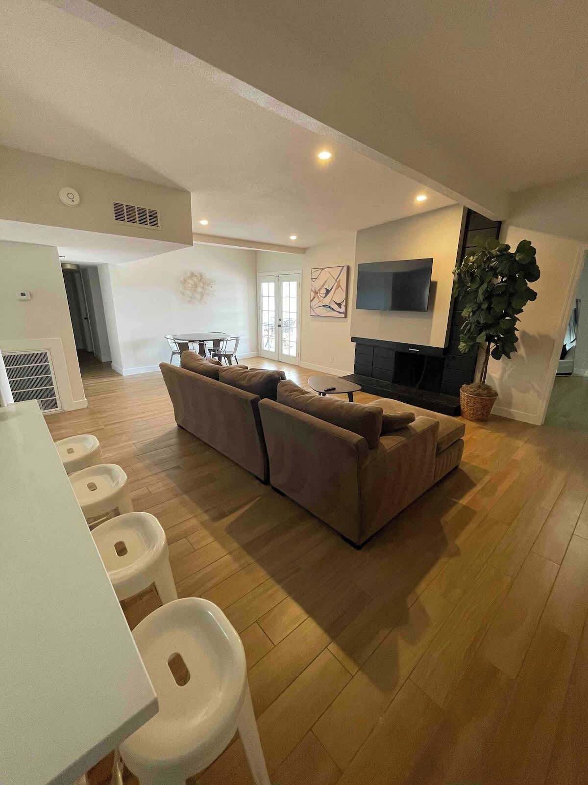 A spacious living area with a large sofa, a flat-screen TV, and a potted plant.