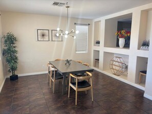 A dining area with a dark wooden table and chairs, a hanging light fixture, and a potted plant. - Peaceful Paradise W/ Pool (Las Vegas)
