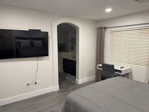 Ein Schlafzimmer mit Bett, Schreibtisch, Fernseher und einem Fenster mit Jalousien.