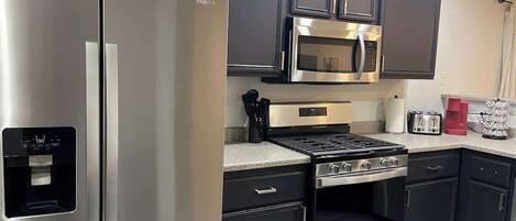 A modern kitchen with stainless steel appliances, dark cabinetry, and a built-in microwave.