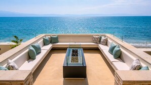 A sunlit outdoor seating area with a view of the sea, a glass coffee table, and a stone balustrade. - Beachfront condo | Beautiful with amenities (Bucerías)