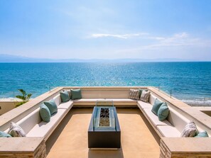Ein sonnendurchfluteter Außenbereich mit Meerblick, einem Glastisch und einer Steinbalustrade.