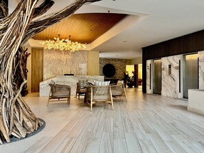 A spacious lobby with a high ceiling, a central seating area with wicker chairs, a marble reception desk, and a modern chandelier. - Beachfront condo | Beautiful with amenities (Bucerías)
