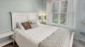 A bedroom with a bed, a nightstand, a lamp, and a window with curtains. - Seaglass Village 225 - Beach House (Wells)