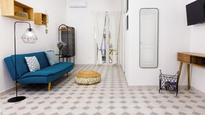 Ett modernt vardagsrum med en blå soffa, en rund pall, en golvlampa, en tv och en hylla i trä.