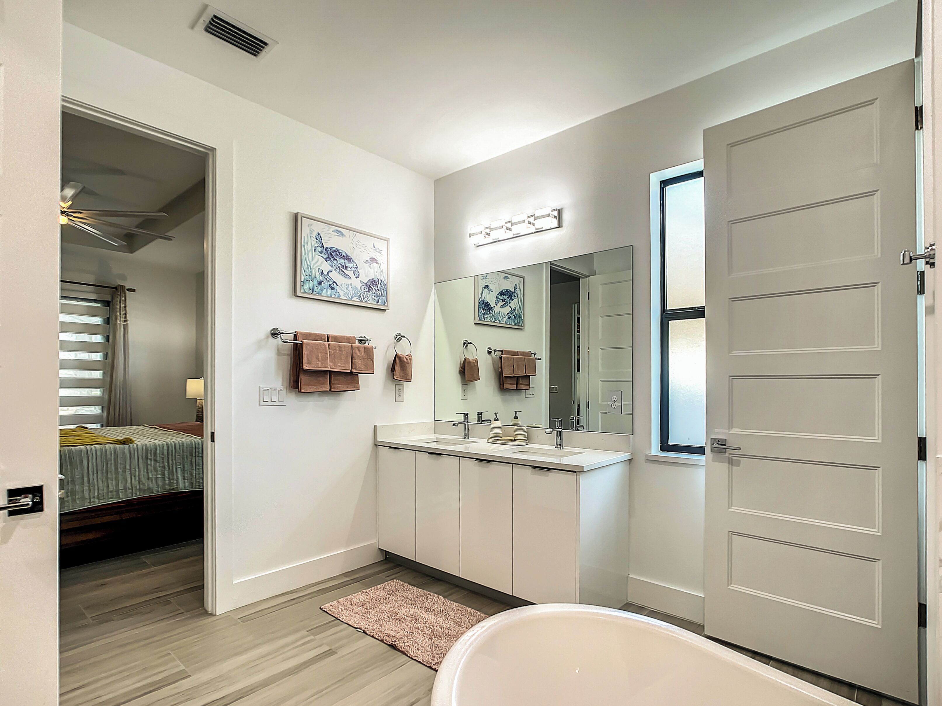 A modern bathroom with a bathtub, a sink, and a mirror. There is a door on the right and a window on the left.