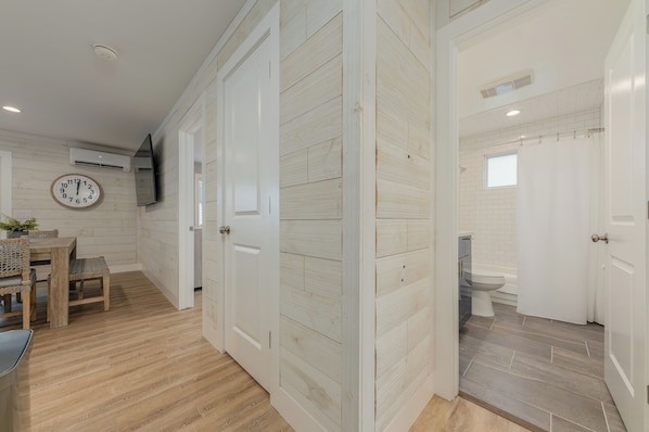 Een hal met houten vloer, een eetgedeelte met tafel en stoelen, en een badkamer met toilet en douche.
