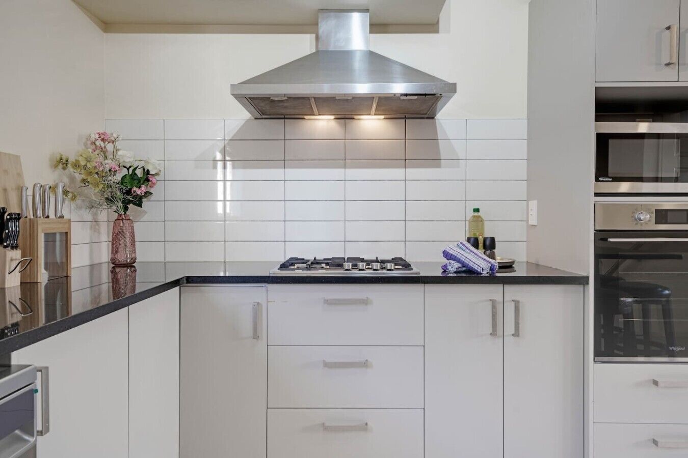 A modern kitchen with white cabinetry, a stainless steel range hood, and a built-in oven.