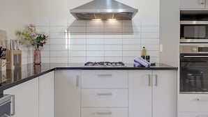 Una cocina moderna con armarios blancos, una campana extractora de acero inoxidable y un horno empotrado.