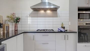 A modern kitchen with white cabinetry, a stainless steel range hood, and a built-in oven.