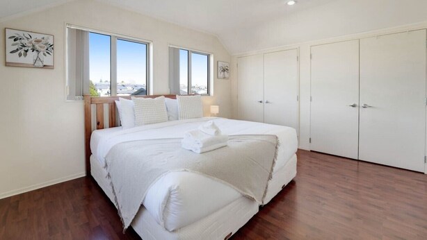 Un dormitorio con una cama grande, dos ventanas, un armario y un cuadro en la pared.
